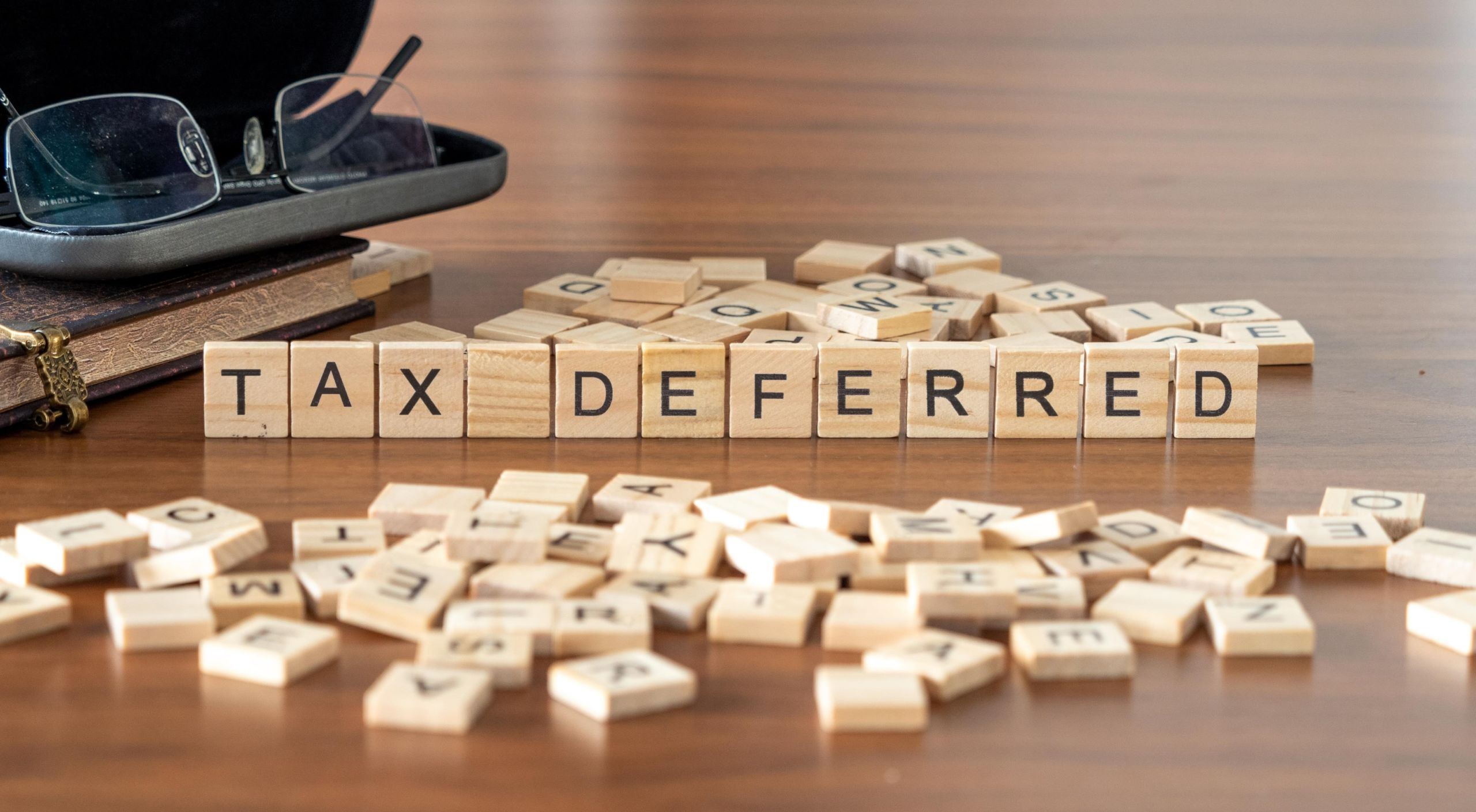 tax deferred word or concept represented by wooden letter tiles on a wooden table with glasses and a book