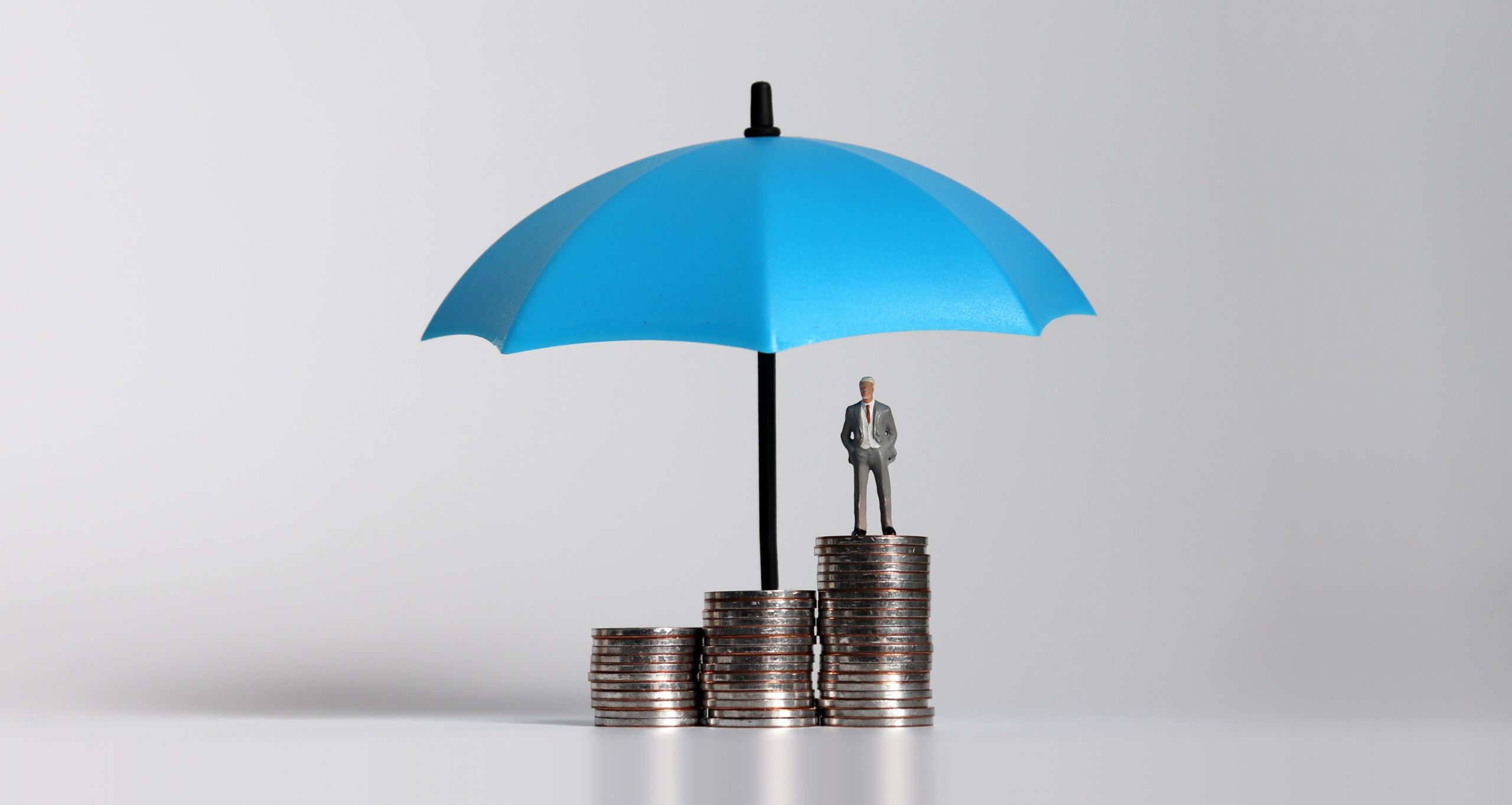 Man standing on a stack of coins that gradually get taller with an umbrella overhead.
